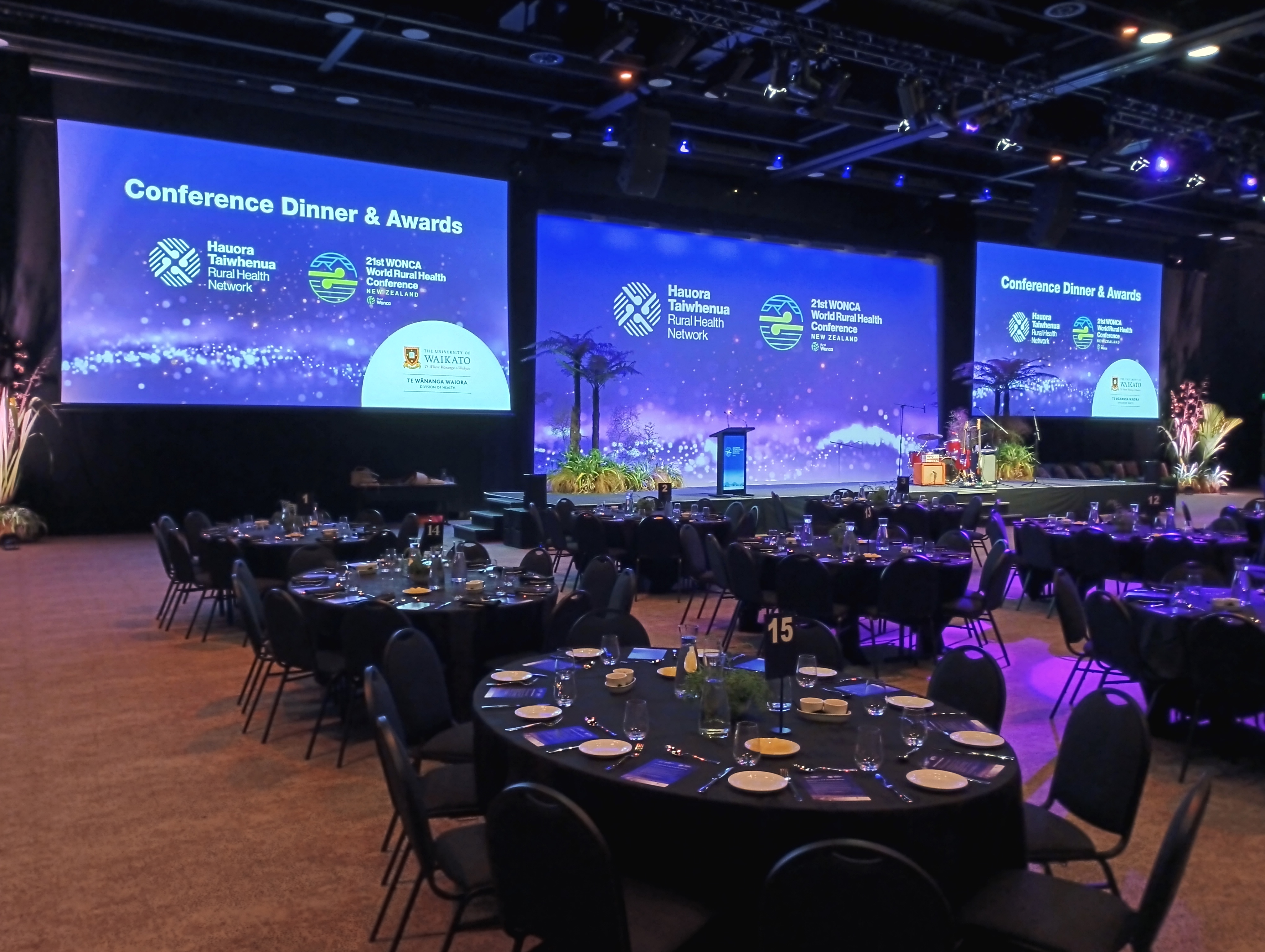 Conference dinner and awards venue with scenic stage screens and banquet tables prepared for guests.
